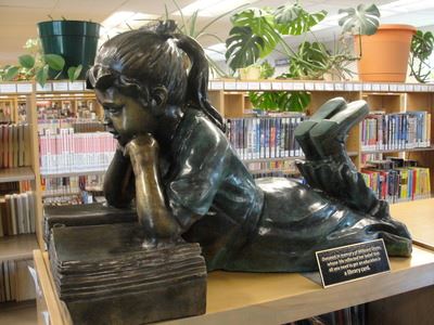 A bronze sculpture of a girl reading a book