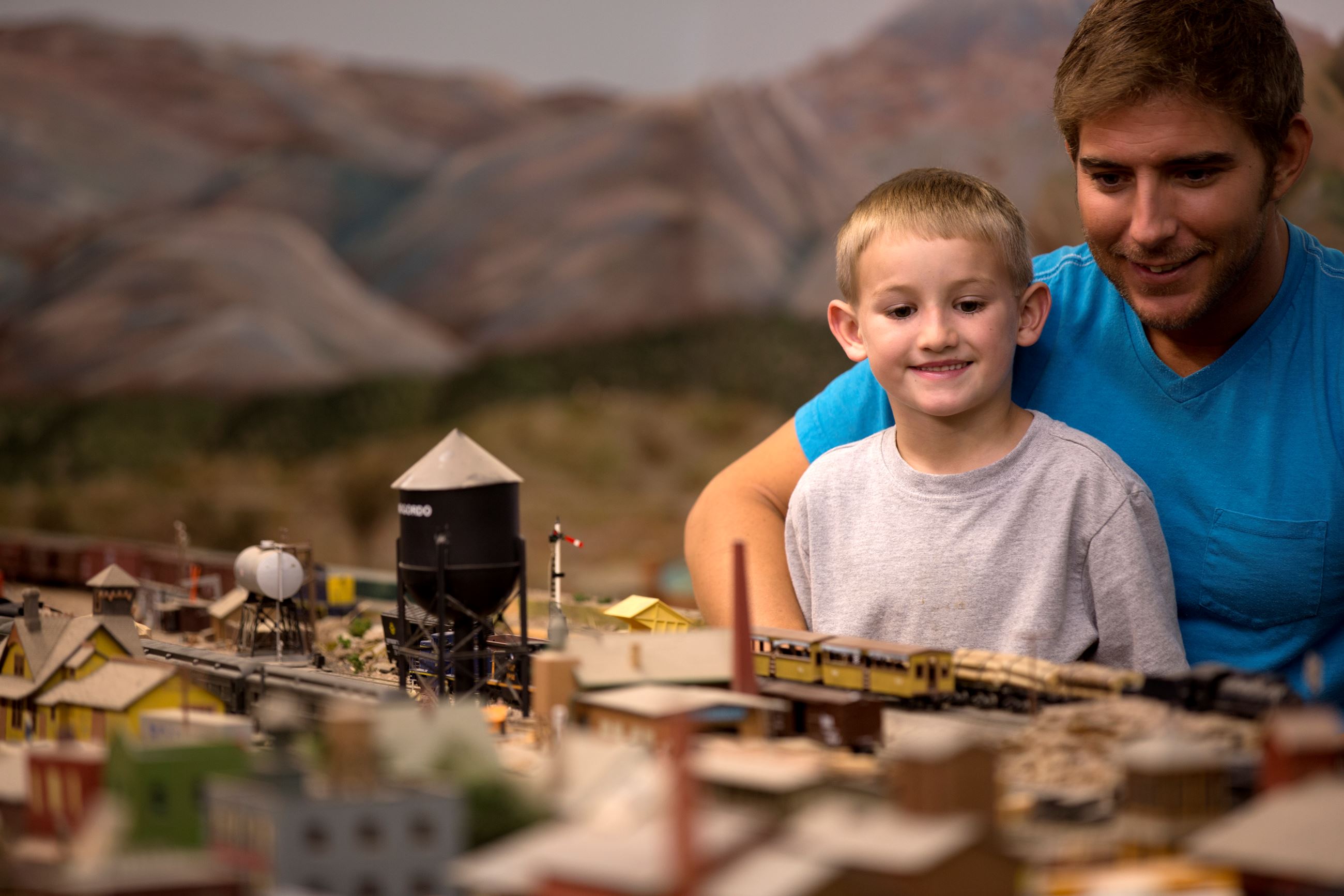 A man and young boy look at a toy train model.
