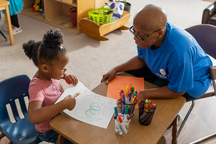 A small child and senior citizen color with markers and crayons at a table. 